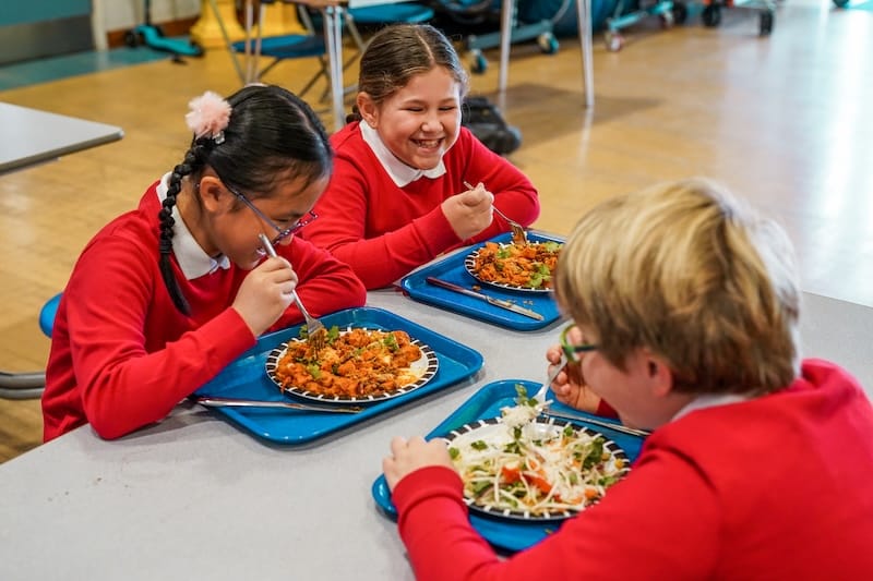 Three children smiling while enjoying healthy school meals.