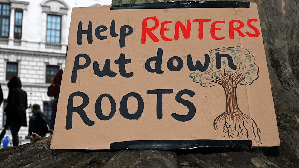 A hand painted placard reads: Help renters put down roots, accompanied by a drawing of a tree.